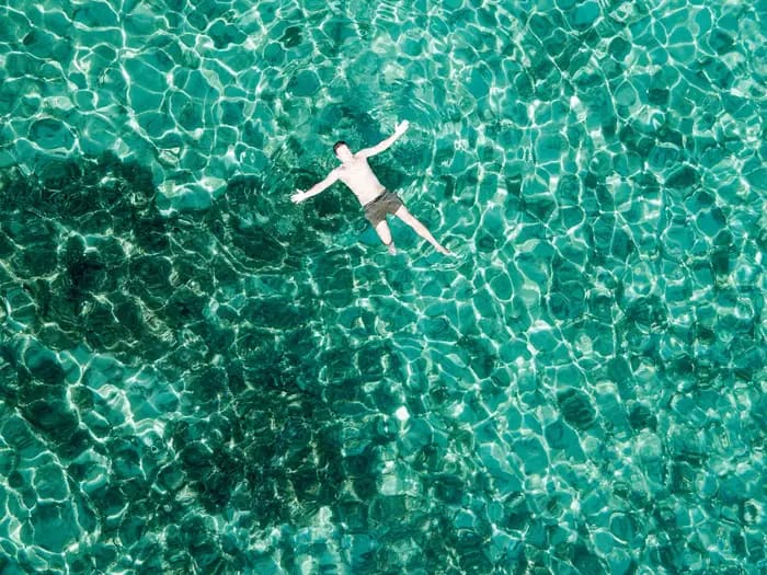 Guest floating in crystal-clear turquoise Adriatic water seen from above
