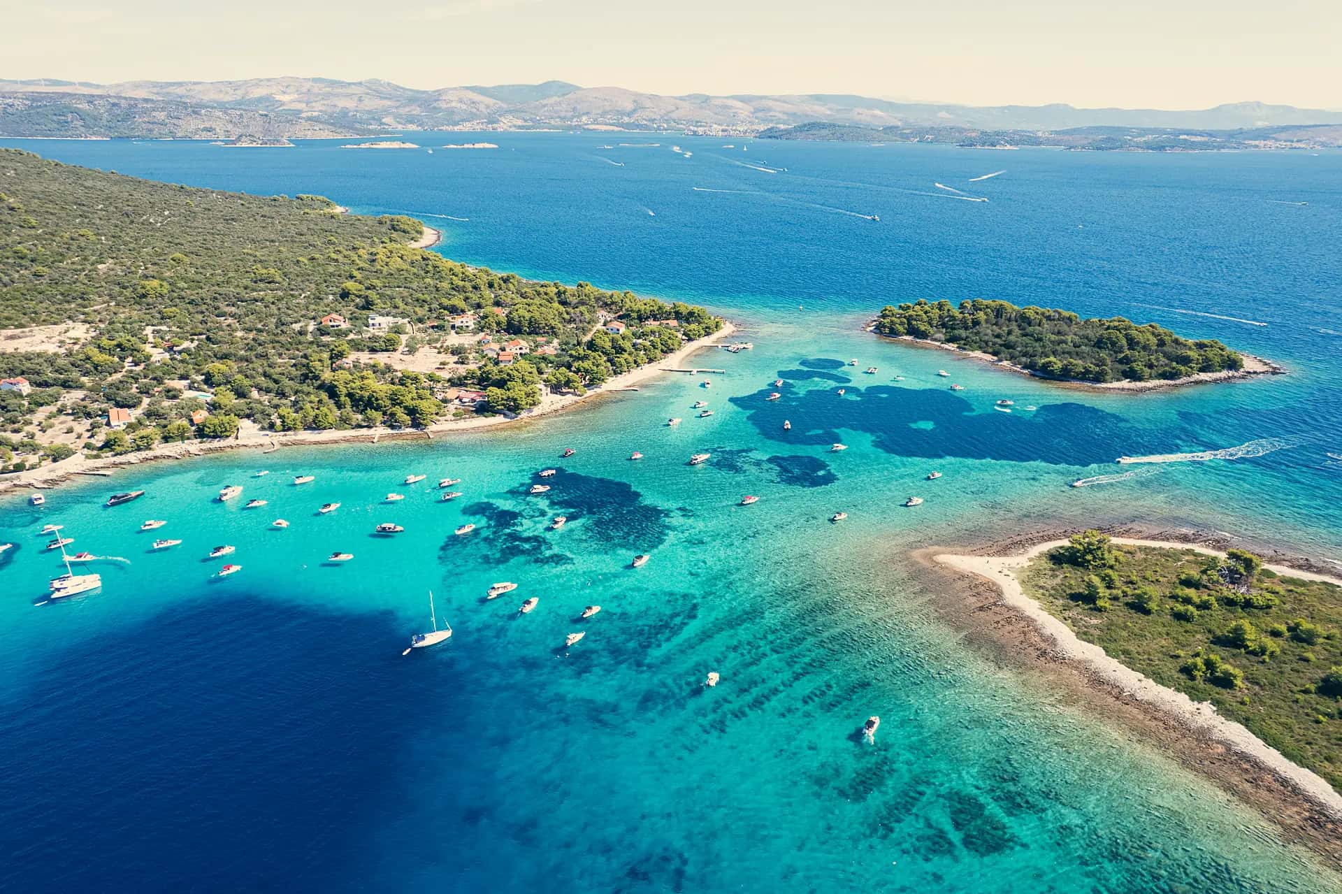 Aerial of the Blue Lagoon near Drvenik, boats anchored over turquoise shallows and dark seagrass, Šolta and the mainland behind